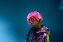 Jovem mulher asiática com corte de cabelo rosa elegante e brilhante jaqueta de prata de pé e desfrutar de música — Fotografia de Stock
