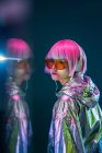 Mulher asiática jovem atraente na moda com cabelo rosa na jaqueta de prata ouvindo música no fundo escuro com reflexão — Fotografia de Stock