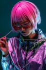 Trendy young Japanese woman with purple hair standing in sparkly silver jacket and red sunglasses on blue background — Stock Photo