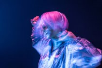 Молодая субкультурная азиатка с розовыми разбросанными волосами и танцующей серебряной курткой под музыку в наушниках — стоковое фото