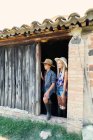 Adolescente chico y hermana de pie en granero entrada juntos en día soleado en granja - foto de stock