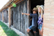 Teen boy pointing at distance for sister while standing in barn entrance together on sunny day on farm — Stock Photo