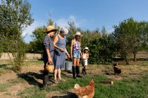 Grandmother with bucket on lawn while standing near grandchildren on sunny day on ranch — Stock Photo