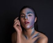 Giovane donna attraente con pittura blu e argento faccia a colori su sfondo nero guardando la fotocamera — Foto stock
