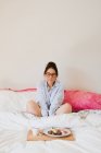 Retrato de mujer con los ojos cerrados mientras está sentada en la cama frente a una bandeja con comida saludable - foto de stock
