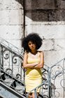 Afrikanische Amerikanerin in gelbem Kleid steht an Geländer gelehnt und blickt vor städtischem Hintergrund in die Kamera — Stockfoto