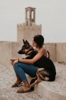 Lässige junge Frauen sitzen mit entzückendem Schäferhund auf Betonpflaster — Stockfoto