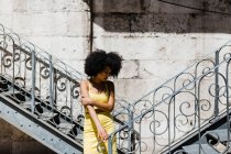 Donna afroamericana in tuta gialla in piedi vicino ringhiera e guardando giù su sfondo urbano — Foto stock