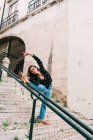 Young slim casual woman stretching and dancing on stairway while dancing gracefully on street of old city — Stock Photo