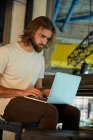 Молодой бородатый красивый мужчина сидит и работает на ноутбуке — стоковое фото