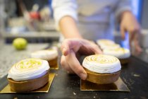 Unerkennbare Hände halten einen köstlichen Baiser-Kuchen in die Auslage einer Bäckerei — Stockfoto