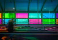 Blurred person with suitcase on mowing walkway near colorful panels inside Madrid Barajas Airport in Spain — Stock Photo