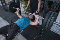 From above young guy exercising with barbell with help of unrecognizable trainer during training in outdoor gym — Stock Photo