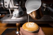 Dall'alto mani di raccolto di dipendente professionale che prepara il cappuccino con modello in cima in caffetteria — Foto stock