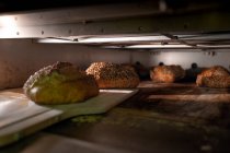 Brotlaibe mit knuspriger Kruste aus heißem Ofen auf großem hölzernen Schulterblatt herausnehmen — Stockfoto