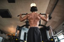 Muscular guy doing pull ups on exercise machine — Stock Photo
