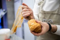 Crop man in apron and white uniform stuffing fresh croissant with chocolate cream indoors — Stock Photo