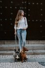 Femme moderne à la mode avec bouledogue et chien debout sur le trottoir de la rue et regardant loin — Photo de stock