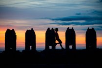 Silhouette of unrecognizable woman standing leaning on rectangular stone sculptures in gloomy breathtaking sunset sky — Stock Photo