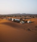 Vista de tiendas de campaña blancas entre pocos árboles verdes en la arena del desierto en Marruecos - foto de stock