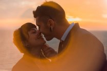 Vista lateral do casal jovem romântico se ligando e beijando em luz do pôr do sol suave no navio em mar calmo — Fotografia de Stock