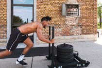 Seitenansicht eines hemdlosen Afroamerikaners, der beim Training im Outdoor-Fitnessstudio schwere Gewichte zieht — Stockfoto