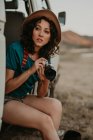 Attraktive junge Frau sitzt im Sommer in einem coolen Van und hält eine Fotokamera mitten im Nirgendwo — Stockfoto