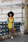 Femme afro-américaine en costume jaune et veste en denim debout et regardant la caméra sur fond urbain — Photo de stock
