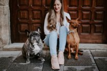 Trendige moderne Frau mit Bulldogge und Hund auf dem Bürgersteig und an Holztür gelehnt — Stockfoto