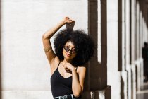 Junge ethnische Frau in Jeans und Tank-Top lehnt an der Wand und blickt in die Kamera im Freien — Stockfoto