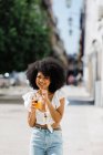 Веселий модний афроамериканець жінка п'є апельсиновий сік і дивлячись на камеру на міському фоні — стокове фото