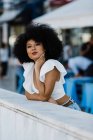 Joven mujer afroamericana en jeans y pensamiento top de la cosecha apoyada en barandilla de piedra al aire libre - foto de stock