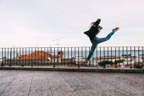 Jovem mulher casual voando em divisões enquanto dança no fundo da cidade costeira — Fotografia de Stock