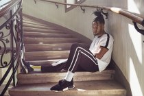 Красивый афроамериканец с плетеными волосами сидит на лестнице и смотрит в сторону — стоковое фото