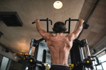 Muscular guy doing pull ups on exercise machine — Fotografia de Stock