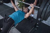 Junger starker Mann hebt Langhantel mit Trainer — Stockfoto