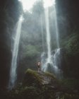 Turista em rocha sob cachoeira nebulosa — Fotografia de Stock