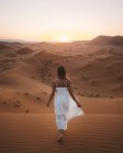 Rückansicht von barfüßigen Frauen in weißem Sommerkleid, die auf einer Sanddüne in der endlosen Wüste im Sonnenuntergang spazieren, Marokko — Stockfoto