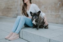 Casual giovane donna seduta su marciapiede di cemento con bulldog sulla strada — Foto stock