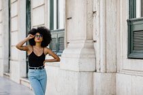 Young ethnic woman in jeans and tank top walking and smiling at camera outdoors — Stock Photo