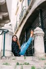 Giovane donna casuale seduta su vecchie scale gambe di sollevamento su pilastro di pietra e guardando la fotocamera — Foto stock