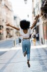 Вид ззаду щасливої етнічної жінки в модному вбранні стрибає з радістю в літній день — стокове фото