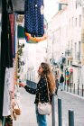 Молода жінка дивиться на барвистий одяг для продажу, стоячи на стійці на вулиці старого міста — стокове фото