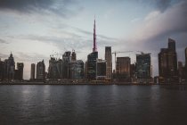 Paisaje urbano de Dubai con majestuosos rascacielos iluminados sobre el agua de la bahía al atardecer - foto de stock
