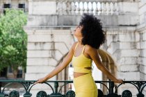 Sensuelle afro-américaine en costume jaune debout et regardant loin sur fond urbain — Photo de stock