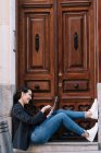 Вид сбоку красивой женщины с цифровым планшетом, расслабляясь на пороге старой деревянной двери — стоковое фото