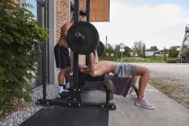 Young guy lifting barbell on street with help of trainer — Fotografia de Stock