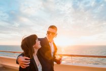 Jovem casal atraente beber bebida vermelha com palhas de um copo no fundo do mar por do sol — Fotografia de Stock