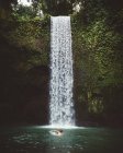 Vista lateral del hombre nadando en aguas cristalinas del lago con cascada en el fondo, Bali - foto de stock