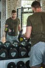 Homme fort faisant de l'exercice avec des haltères au gymnase devant un miroir — Photo de stock